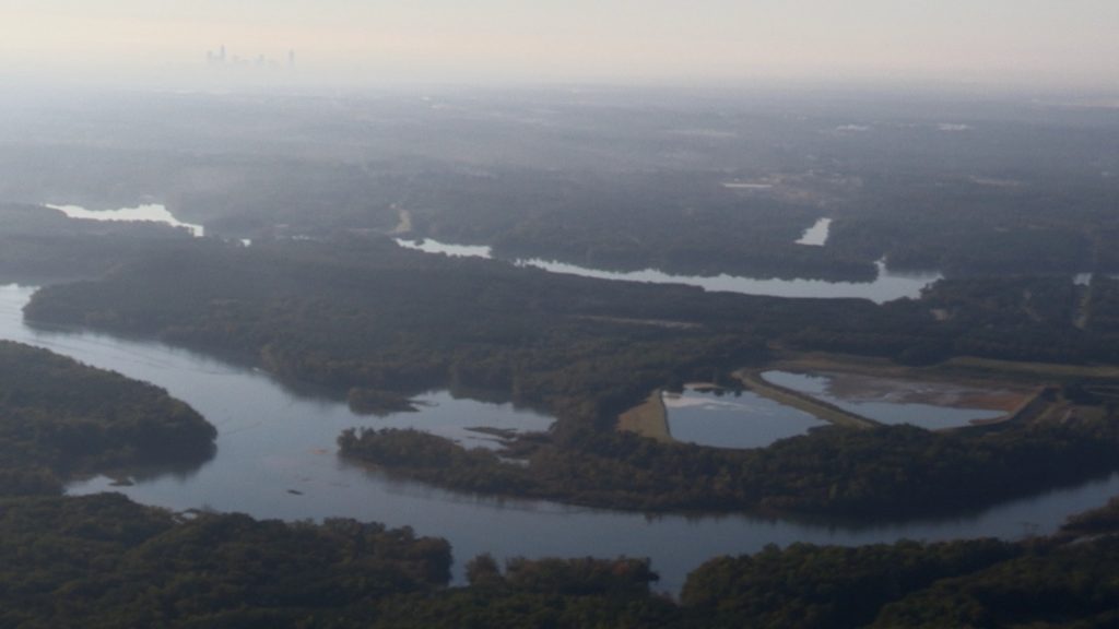 Film still from Downwind and Downstream: With Power Comes Responsibility. Coal ash impoundments along the Catawba River with the Charlotte skyline.